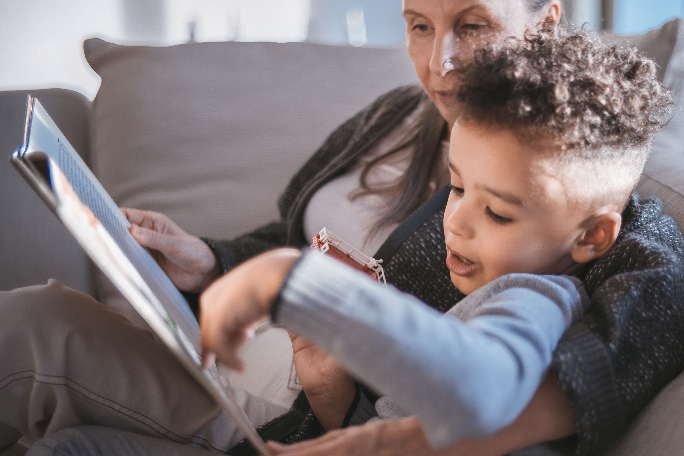 A grandmother and a young child reading together on a sofa